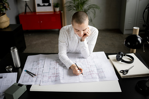 Young bald student woman thoughtfully doing blueprints on her desk