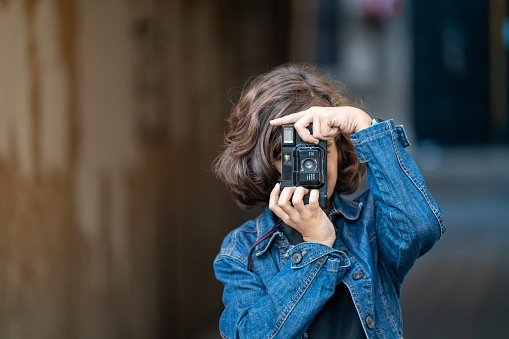 Photo of 9 years old boy photographing via old fashioned analog film camera in outdoor. Selective focus on model. Shot in outdoor with a full frame mirrorless camera.