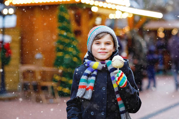 istock Little cute kid boy eating white chocolate covered fruit apple on skewer on traditional German Christmas market. Happy child on traditional family market in Germany during snowy day. 1436088293