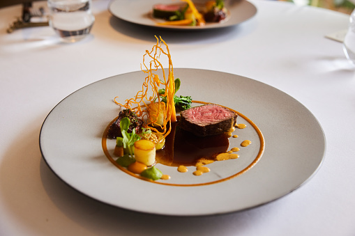 Close-up of an elegant beef main dish sitting on a plate on a table in a fine dining restaurant
