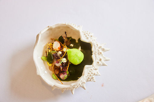 High angle view of an elegant dish of food plated in ashell-shaped bowl on a table in a fine dining restaurant
