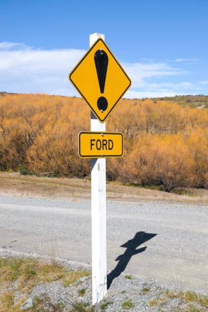 Ford Warning Post Road sign warning of a stream crossing ahead.  The sign has bullet holes from gun shots.  This image was taken near Lake Pukaki on a sunny afternoon in early Spring. ford crossing stock pictures, royalty-free photos & images