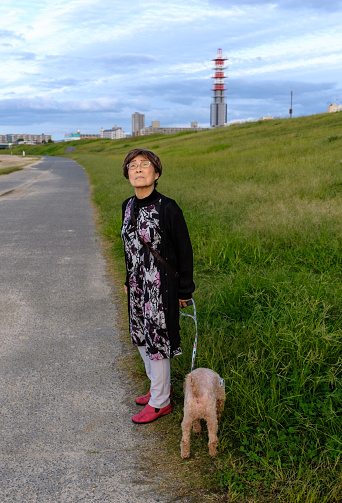 A senior woman standing with a dog outside.
