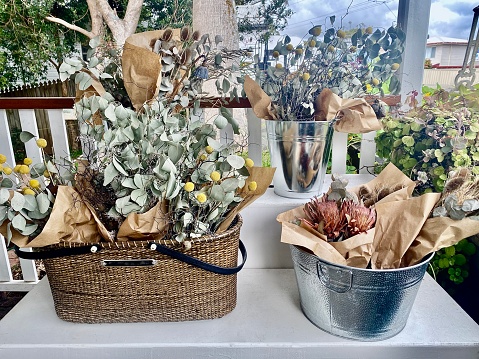Horizontal still life of country garden flower baskets including eucalyptus leaves and dried arrangements on outdoor table