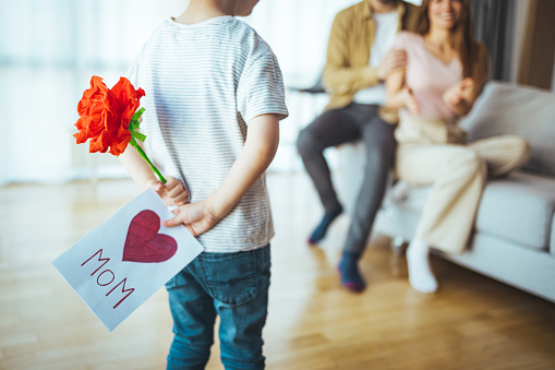 Cute little boy son congratulating his mom happy woman with Mothers day, giving her handmade greeting postcard with red heart at home. Family holidays concept.  International Women's Day or special event at home.