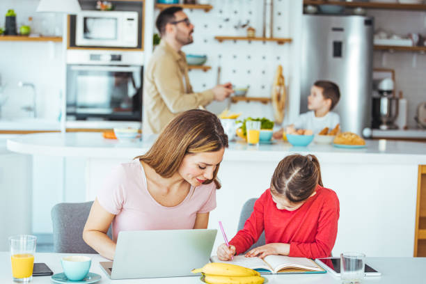 photo d’une jeune mère caucasienne aux cheveux bruns qui aide sa fille à faire ses devoirs devant le bureau sur pied. - women computer home interior brown hair photos et images de collection