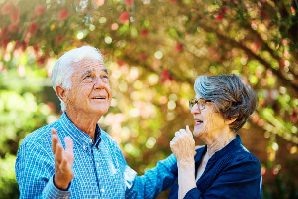 Elderly couple in their 70s have an amusing interaction outdoors in a sunny garden Senior couple having a playful conversation outdoors during the day. rolling eyes irritation displeased facial expression stock pictures, royalty-free photos & images