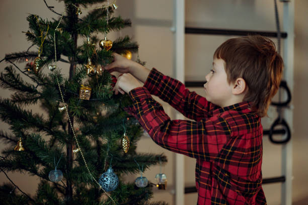 istock Little cute caucasian boy decorating Christmas tree with twinkling decorations. 1436098670