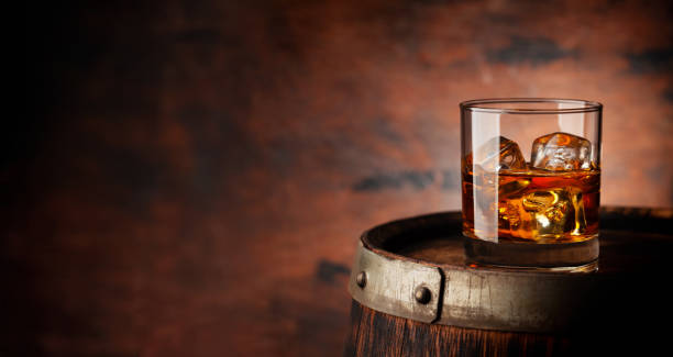 Glass of whiskey with ice cubes on the old barrel Glass of whiskey with ice cubes on the old barrel. With copy space on wooden background bourbon whiskey stock pictures, royalty-free photos & images