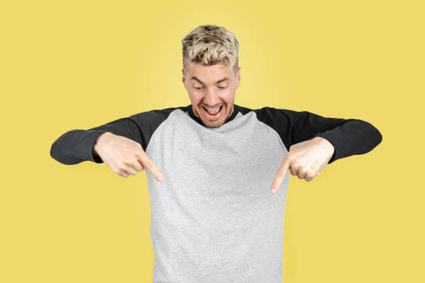 Surprised Caucasian man pointing fingers and looking down at space for advertising, promotion or offer. Yellow background stock photo