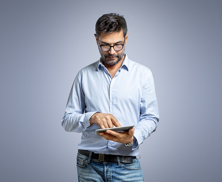 Front view of serious man in eyeglasses typing on his tablet computer. Digital communication concept.