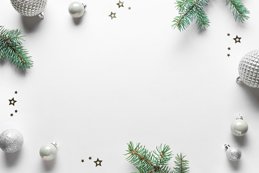 Christmas Decorations and Pine Branches frame on white background, top view, copy space. Festive Christmas seasonal trendy composition with silver ornaments.