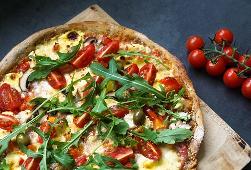 Freshly baked whole-grain sesame pizza with arugula, tomato, olive, mushroom, hollandaise sauce and mozzarella