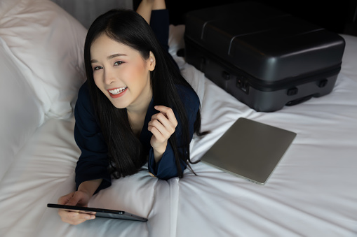 Business Technology Internet Hotel Vacation Concept Happy young businesswoman holding tablet computer lying down on bed Beautiful young business woman looking at camera enjoy vacation time at Hotel