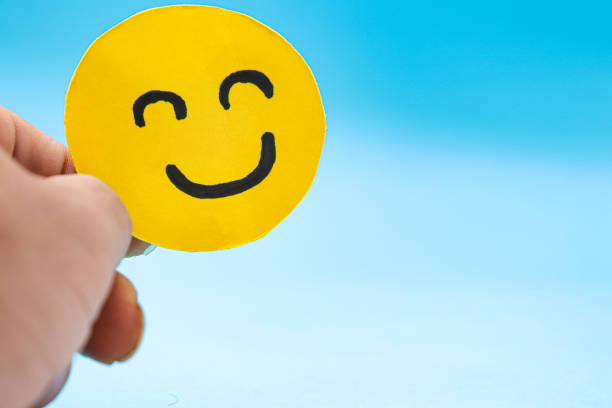 istock Hands holding smiley yellow paper face on a blue background. Happiness concept, positive thinking, mental health assessment, world mental health day concept, optimism 1436112302