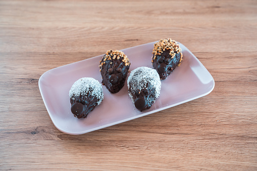 Four pieces of chocolate coated cakes in shape of a hedgehog. Sprinkled with crushed almonds and coconut flakes. Displayed on white ceramic plate put on wooden table.