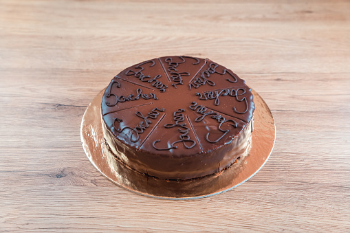 Full, round shaped Sacher cake with writing on each piece to be cut, displayed on a wooden table, high angle view. Full length image.