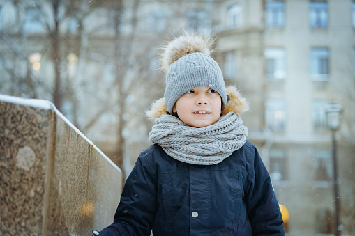 winter portrait of cute caucasian 7 years old boy in knit hat with pompom in city. Image with selective focus
