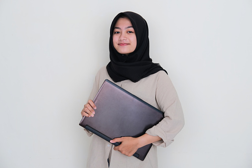 Young Asian girl wearing hijab smiling to camera while holding a laptop