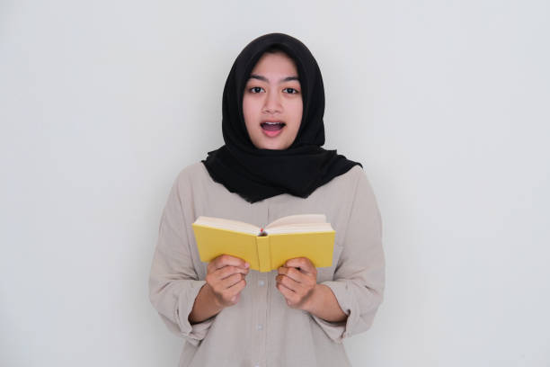 istock Young girl wearing hijab showing shocked expression while holding a book 1436114007
