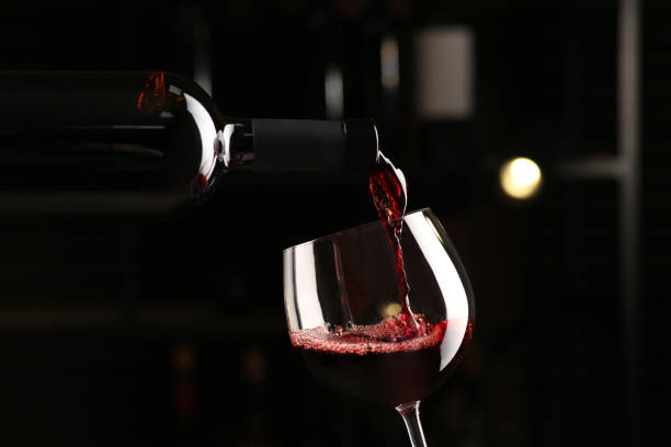 istock Pouring red wine from bottle into glass on blurred background, closeup 1436115946