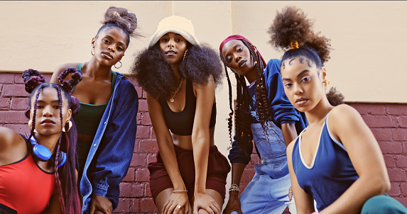 Group of trendy women in city, friends model urban futuristic fashion and creative funky New York style. Designer clothing with jewelry, afro hair aesthetic and cool portrait on brick wall background