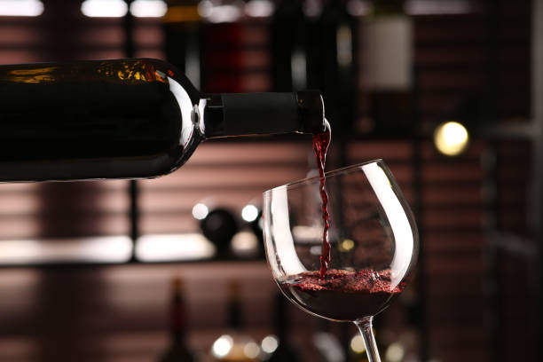 istock Pouring red wine from bottle into glass on blurred background, closeup 1436116433