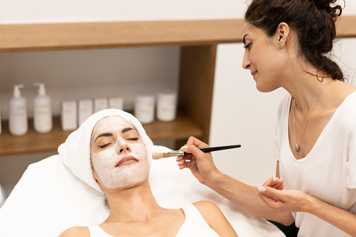 Aesthetics applying a mask to the face of a Middle-aged woman in modern wellness center. Beauty and Aesthetic concepts.