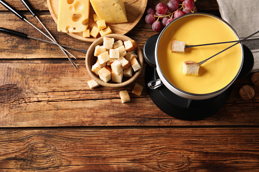 Pot of tasty cheese fondue and snacks on wooden table, flat lay. Space for text