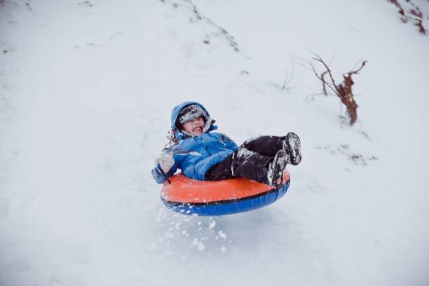 Boy sliding down hill on a snow tube - fotografia de stock