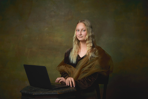 Aspiration. Young charming girl in image of Mona Lisa, La Gioconda using laptop isolated on dark green background. Creative art, beauty, style, imitation, eras comparison