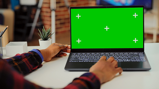 African american woman looking at greenscreen on laptop at desk, working with isolated display and mockup template on wireless pc. Using portable computer with blank copyspace.