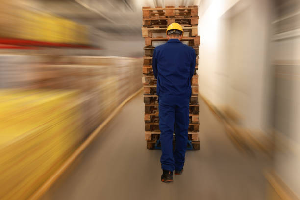 istock Worker moving wooden pallets with manual forklift in warehouse, back view 1436122437