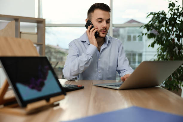 istock Forex trader talking on phone while working with laptop in office 1436122590