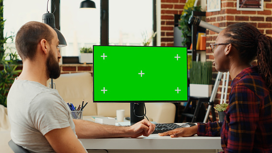 Diverse people working with greenscreen monitor on computer, analyzing isolated chroma key on blank background. Planning teamwork at home office desk using mockup copyspace template.