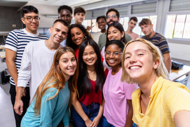 Multiracial group of student friends taking selfie with teacher in classroom stock photo
