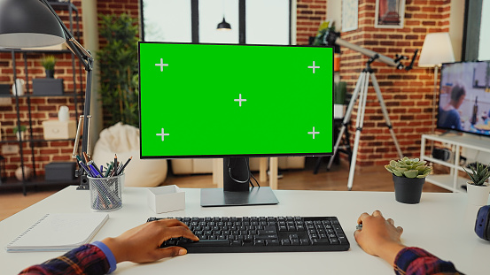 Office worker analyzing isolated greenscreen on computer to work with chroma key display on monitor. Looking at blank copyspace and mockup to use keyboard and desktop. Tripod shot.