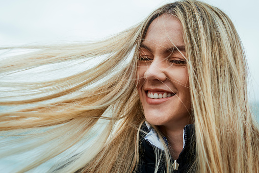 Face of woman with wind in hair and happy on relax holiday vacation for peace, calm and outdoor freedom in Canada. Happiness, hair care and young beauty girl or gen z teen student on gap year travel