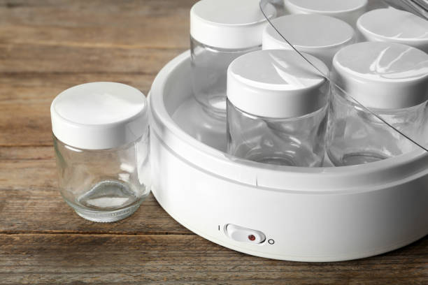 istock Modern yogurt maker with empty jars on wooden table, closeup 1436130187