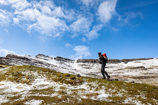 Man hiking in Scotland, Isle of Skye, with snowy mountains on background - Hiker climbing up a ridge on a winter day - Travel and adventure concepts