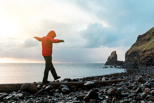 Man hanging in the balance over a log at seaside in Scotland - Hiker having fun at beautiful destination Talisker bay after the rain - Filter applied, travel and adventure concepts