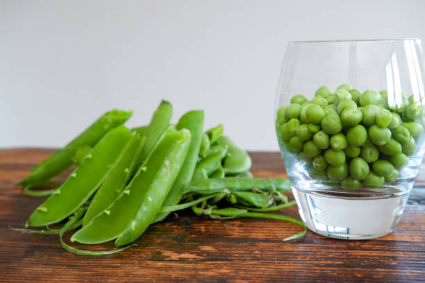 green peas in glass bowl. fresh pea in the pod with green leaves. green peas on a brown wodden table - green pea pea pod salad legume imagens e fotografias de stock