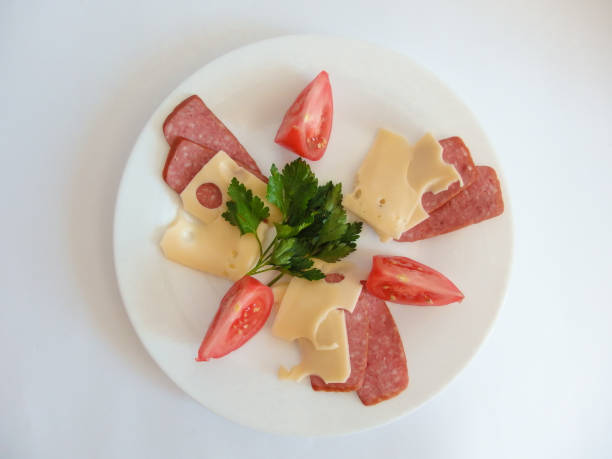 A traditional Romanian lunch with plates of fresh vegetables - spring onions, tomatoes, cucumbers. There is fresh meat including salami, sausage and slanina - cubes of pork fat. There are hard boiled eggs and a loaf of fresh bread. All of this is presented on a white wooden surface.