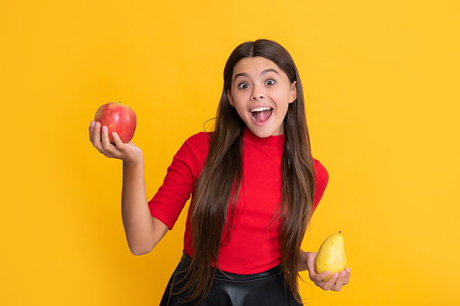 amazed child hold apple and pear on yellow background.