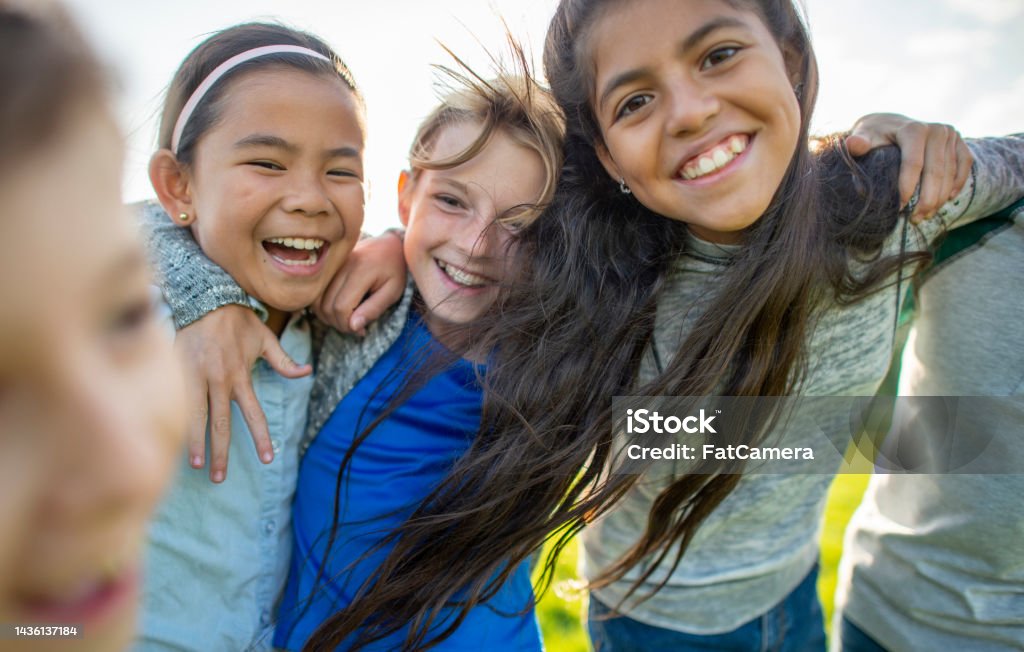 Elementary Friends Outdoors A small group of Elementary children huddle in closely to one another as they pose for a portrait.  They are each dressed casually and are smiling as they spend the time together. Child Stock Photo