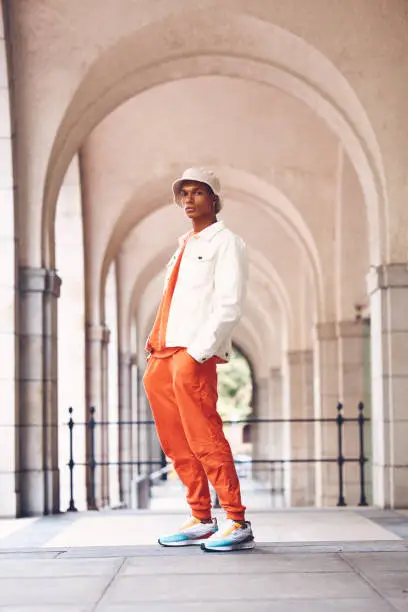 Photo of Fashion portrait, cool and black man posing in a city arch building. Stylish lifestyle, retro and handsome creative person or designer model in fashionable, fancy and edgy hat, shirt and pants.