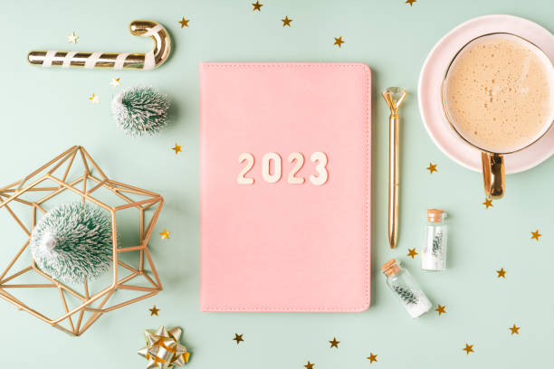 istock Christmas pink notepad with 2023 letters text. Flat lay on green mint table background with planner, cup of coffee, candle, Christmas decoration, notebook and stationery. Top view Desktop. 1436146026