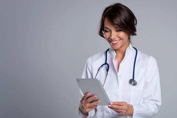 Smiling female doctor with digital tablet standing at isolated grey background stock photo