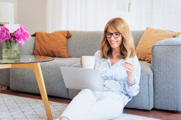 istock Middle aged woman using a laptop and drinking tea while working from home 1436151418