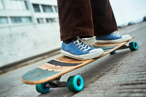 Skateboard, shoes and sport with a skater in the city on a board with balance for sports, fun and recreation. Skating, skill and hobby with an athlete outdoor in a town on a street or road closeup